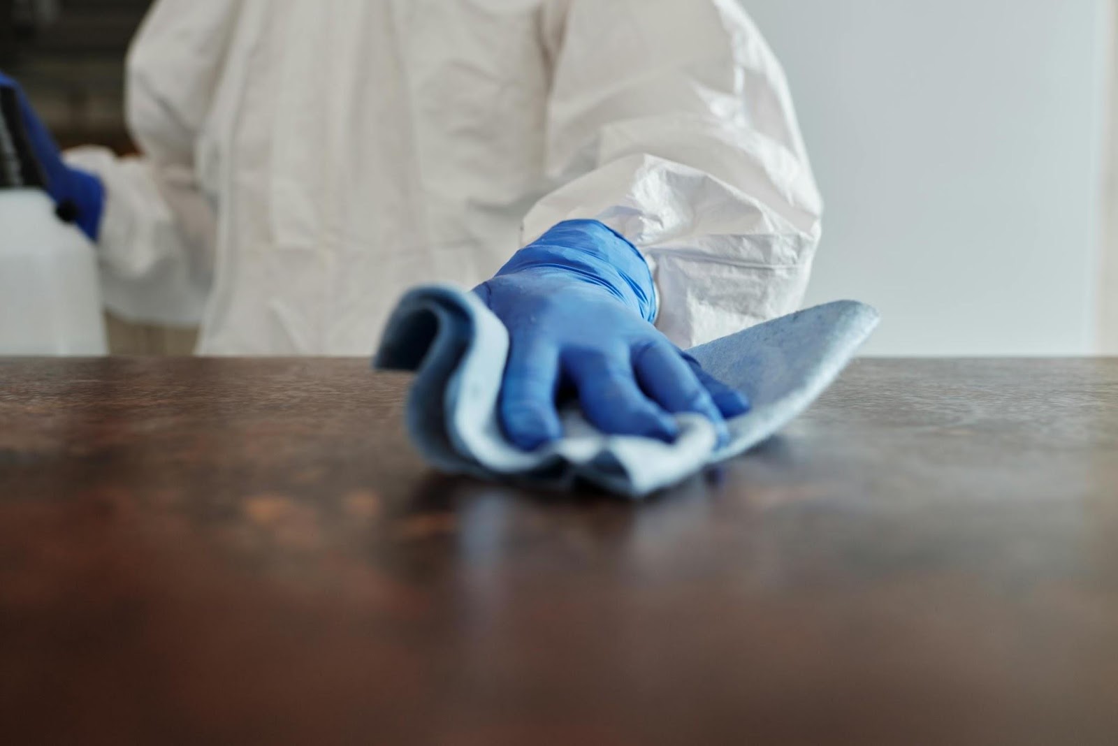 A cleaner in a white coat and blue gloves scrubbing a table, showcasing post-renovation cleaning Singapore.