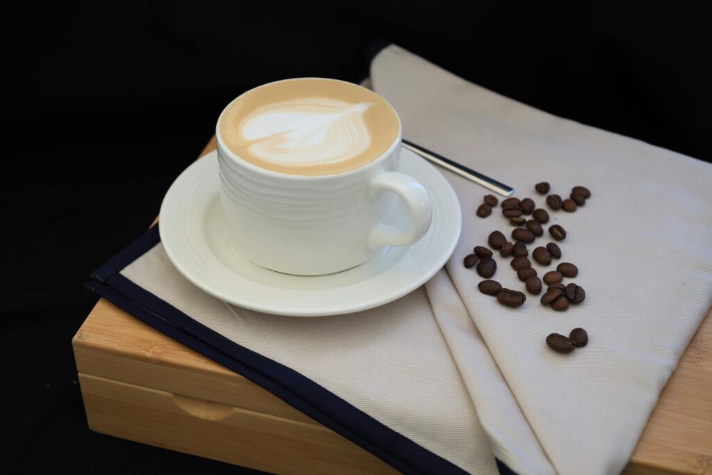 Creamy latte with artistic design in white cup beside scattered coffee beans.