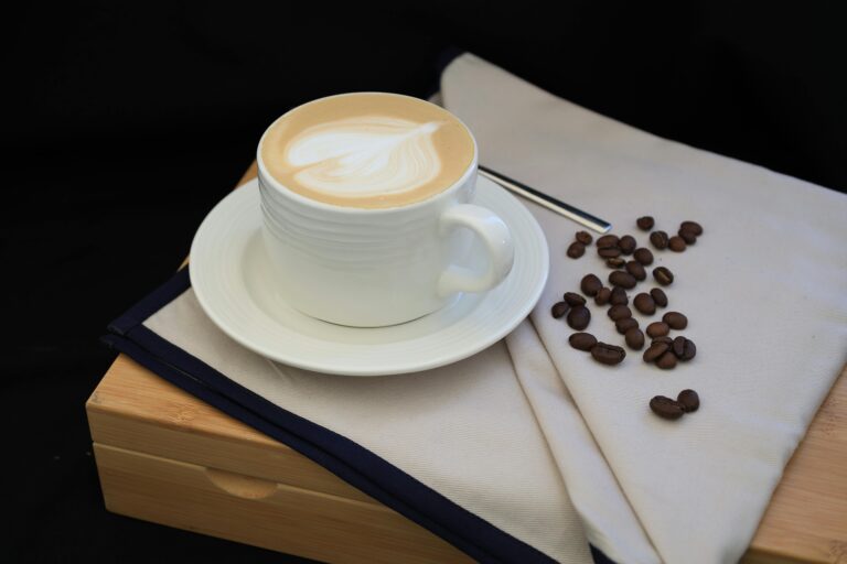 Creamy latte with artistic design in white cup beside scattered coffee beans.