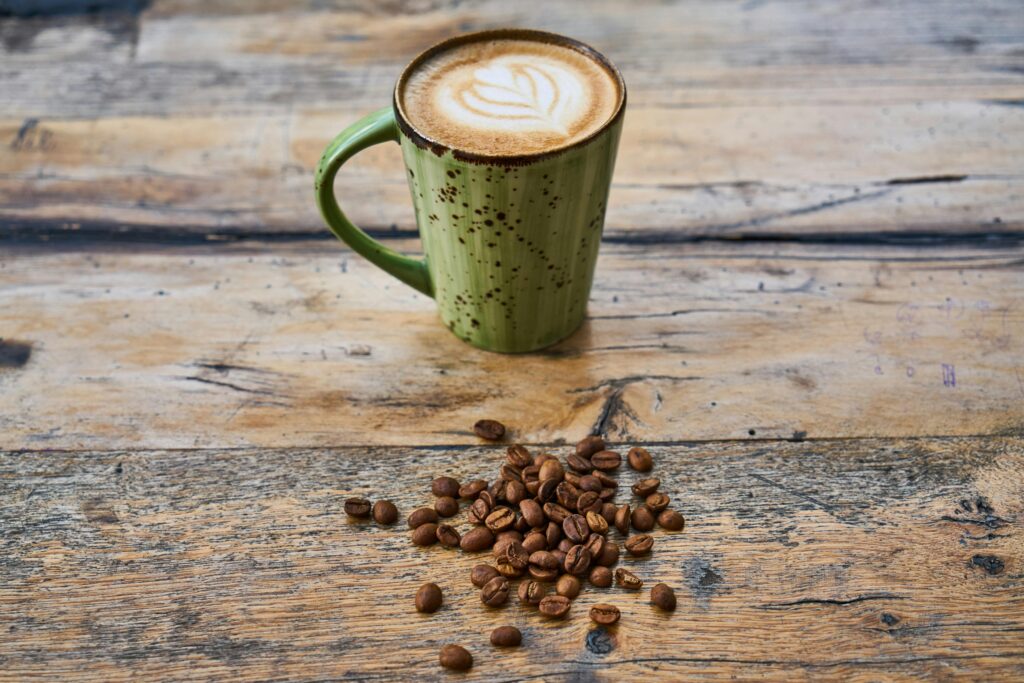A green mug of cappuccino with coffee beans on a rustic wooden surface.
