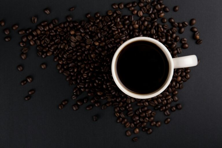 Flat lay of a white coffee mug with black coffee surrounded by roasted coffee beans.