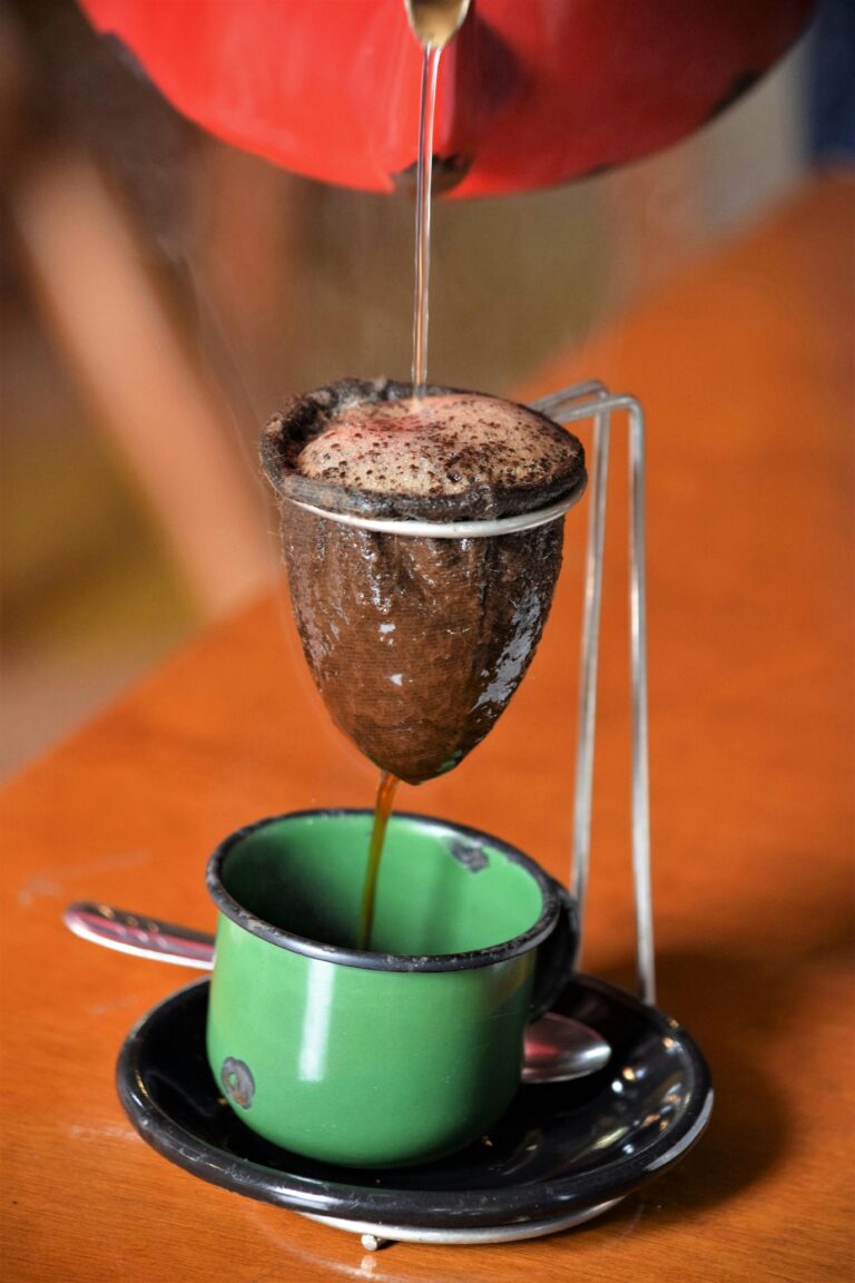 Close-up of traditional Brazilian coffee being brewed with cloth filter into a green cup.